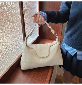 Close-up of litchi texture on off-white leather underarm bag with embossed text detail