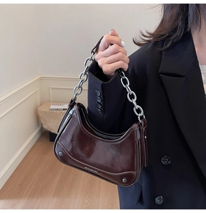 Detail of dark brown glossy leather underarm bag with bold silver metal chain strap