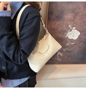 Detail shot of beige lychee pattern leather shoulder bag with fine stitching on blue sweater