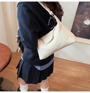Close-up of beige lychee texture leather shoulder bag worn by model in a warm room