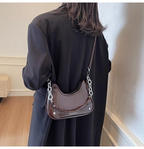 Detail of dark brown semi-circle handbag featuring silver chains and metallic rivets