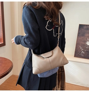 Detail of lychee textured leather crossbody bag in beige worn by a model in soft light