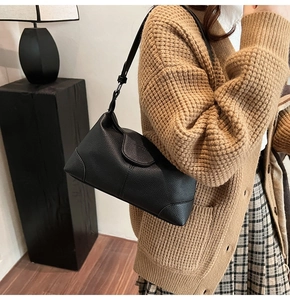 Detail of black pebbled leather underarm bag worn on shoulder by model in cozy interior