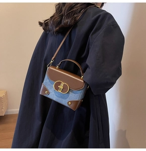 Detail of blue denim and brown leather crossbody bag worn with a black wool coat