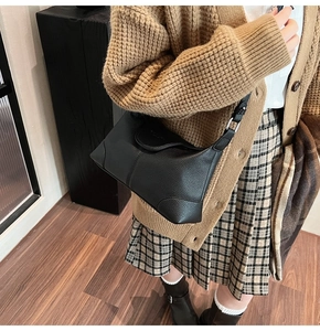 Detail of black pebbled leather crossbody bag paired with autumn plaid skirt and boots