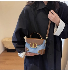 Detail of trendy color-block crossbody bag featuring blue denim and brown leather trim