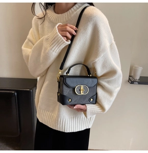 Detail of a structured black crossbody bag with a gold oval clasp on a knit sweater