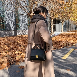 Schwarze strukturierte Lederhandtasche mit goldener Schließe vor beigem Herbstmantel