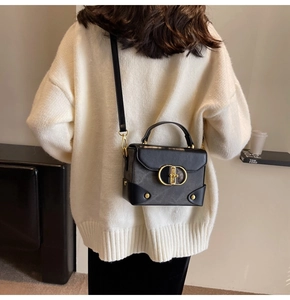 Detail of black box-shaped crossbody bag with gold ring buckle on a white knit sweater