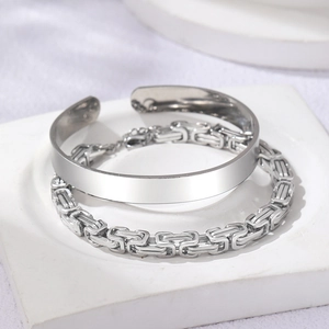 Detailed shot of silver Byzantine chain and wide cuff bracelet on stone pedestal