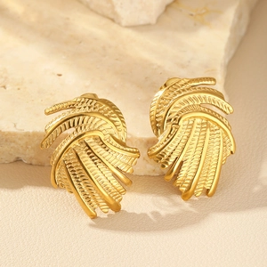Detail of golden spiral earrings with textured feather patterns on a stone base