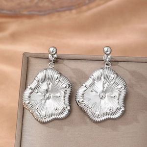Boucles d'oreilles pendantes fleurs argentées avec pétales texturés sur présentoir