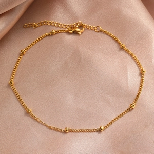 Detail of a gold bead chain anklet with lobster clasp on luxury champagne satin fabric