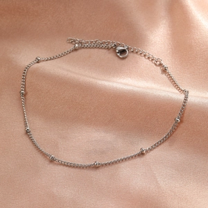 Detail of silver bead chain anklet with lobster clasp on champagne satin fabric