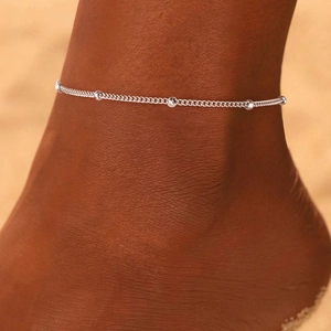 Detail view of a minimalist silver bead anklet worn on ankle during summer vacation