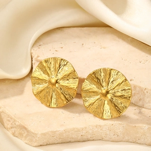 Detailed close-up of gold round earrings with sunburst texture on a cream stone base