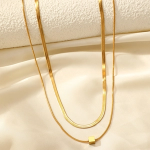 Detail of layered gold snake chain necklace with a cube pendant on silk fabric