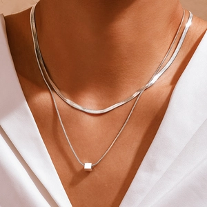 Detail of layered silver snake chains with minimalist cube pendant on woman's neck