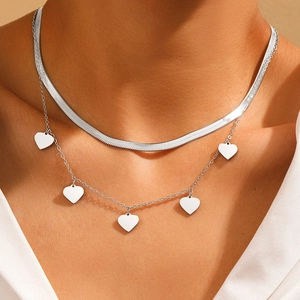Close-up of double layer silver necklace with snake chain and heart charms on model neck