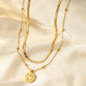 Makroaufnahme einer goldene Doppelkette mit Herzanhänger auf weichem Satinstoff