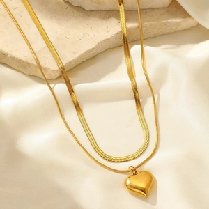 Détail du collier double rang doré avec pendentif cœur sur marbre et tissu satiné