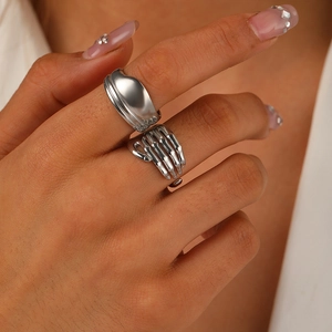 Detail of a minimalist wide silver ring and a unique skull hand ring on a finger