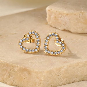 Close-up of heart-shaped gold stud earrings with sparkling pavé crystals on stone base