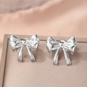 Polished silver bow earrings for women on a textured jewelry tray in elegant warm lighting