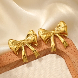 Macro view of polished gold bow earrings on a neutral silk fabric background