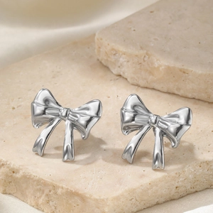 Minimalist silver bow earrings made of polished steel on a beige stone display base