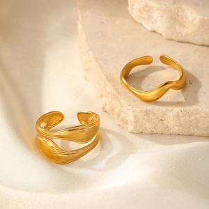 Detail of two adjustable gold wavy rings with liquid metal texture on silk background