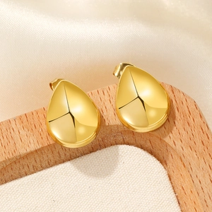 Macro detail of high-polished 18K gold-plated teardrop earrings on a wooden stand