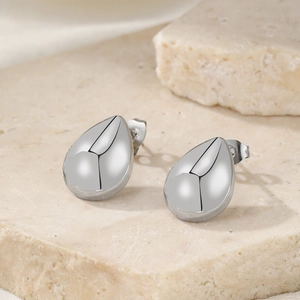 Polished silver teardrop earrings with grooved lines on a natural stone surface