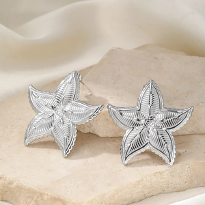 Detailed view of silver starfish earrings with fine ribbed texture on a stone surface