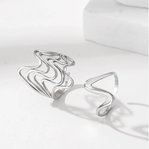 Detail view of silver liquid metal wave rings on white geometric stone backdrop