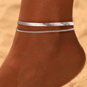 Detail of layered silver snake chain and bead anklet shown on beach background
