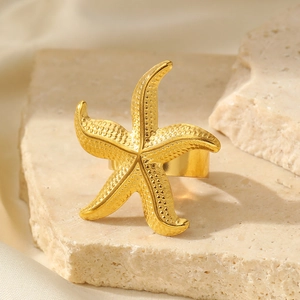 Bague étoile de mer dorée élégante avec texture sur pierre beige et fond de soie