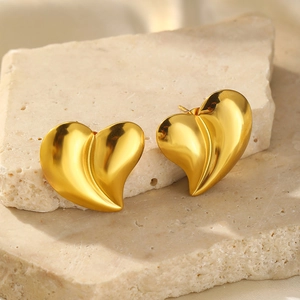 Macro detail of high-polished 18K gold heart-shaped earrings on stone and silk