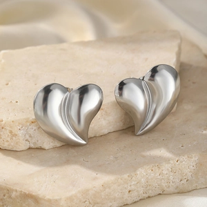 Macro shot of silver heart stud earrings with satin finish on natural stone background