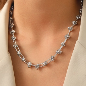 Close-up of a silver-toned knot chain necklace worn with a minimalist beige blazer