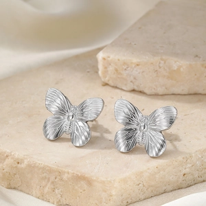 Close-up of silver butterfly stud earrings with radial texture on a stone base