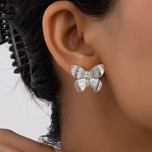 Detail view of silver butterfly earring with textured wings on a female model