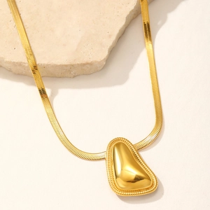 Détail de la chaîne serpent dorée avec pendentif poli sur un support en pierre épuré