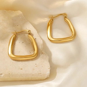 Close-up of gold-plated U-shaped earrings on a natural stone with silk fabric
