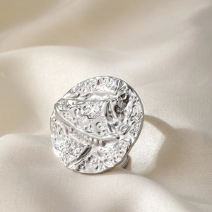 Detailed close-up of textured silver stainless steel hoop earring on white silk background