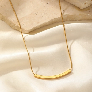 Macro shot of minimalist gold smile necklace with sleek curved pendant on silk and stone