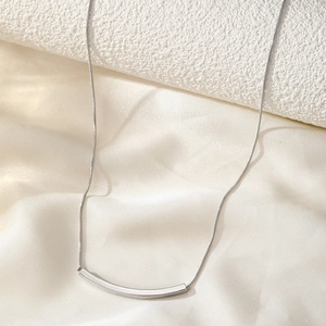 Minimalist silver curved bar necklace with sleek snake chain shown on elegant fabric