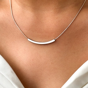 Close-up of a silver minimalist curved bar necklace with a sleek snake chain on a neck