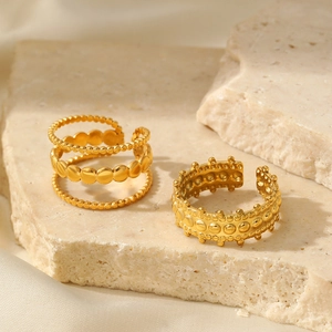 Detail of two irregular gold-plated stainless steel rings on a stone and silk background