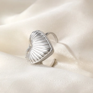 Macro view of silver heart ring featuring textured radial grooves on white satin fabric